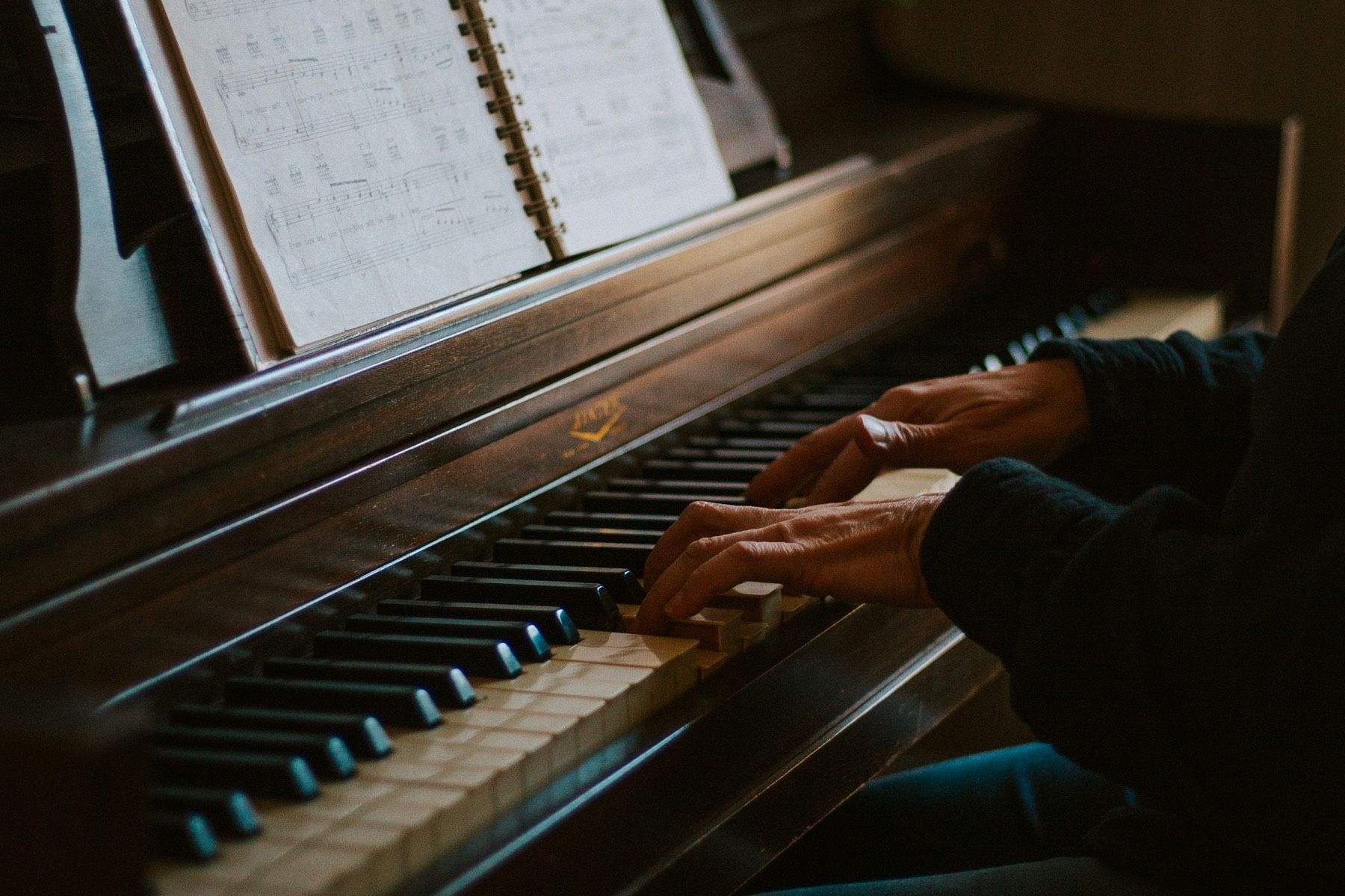 Hände spielen Klavier, links steht ein aufgeschlagenes Notenbuch