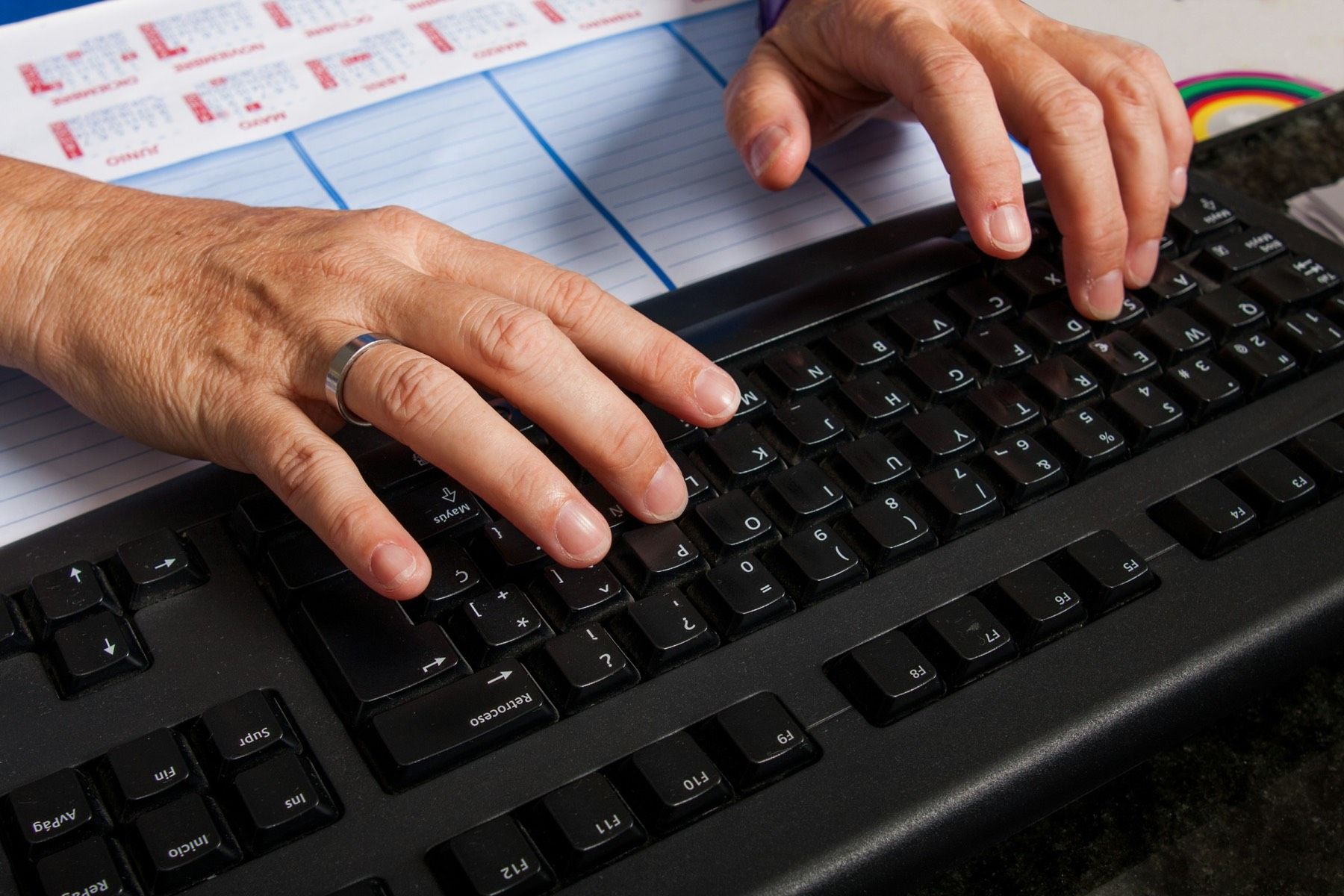Zwei Hände tippen auf einer Tastatur, daneben liegt ein Kalender mit Monatsübersicht